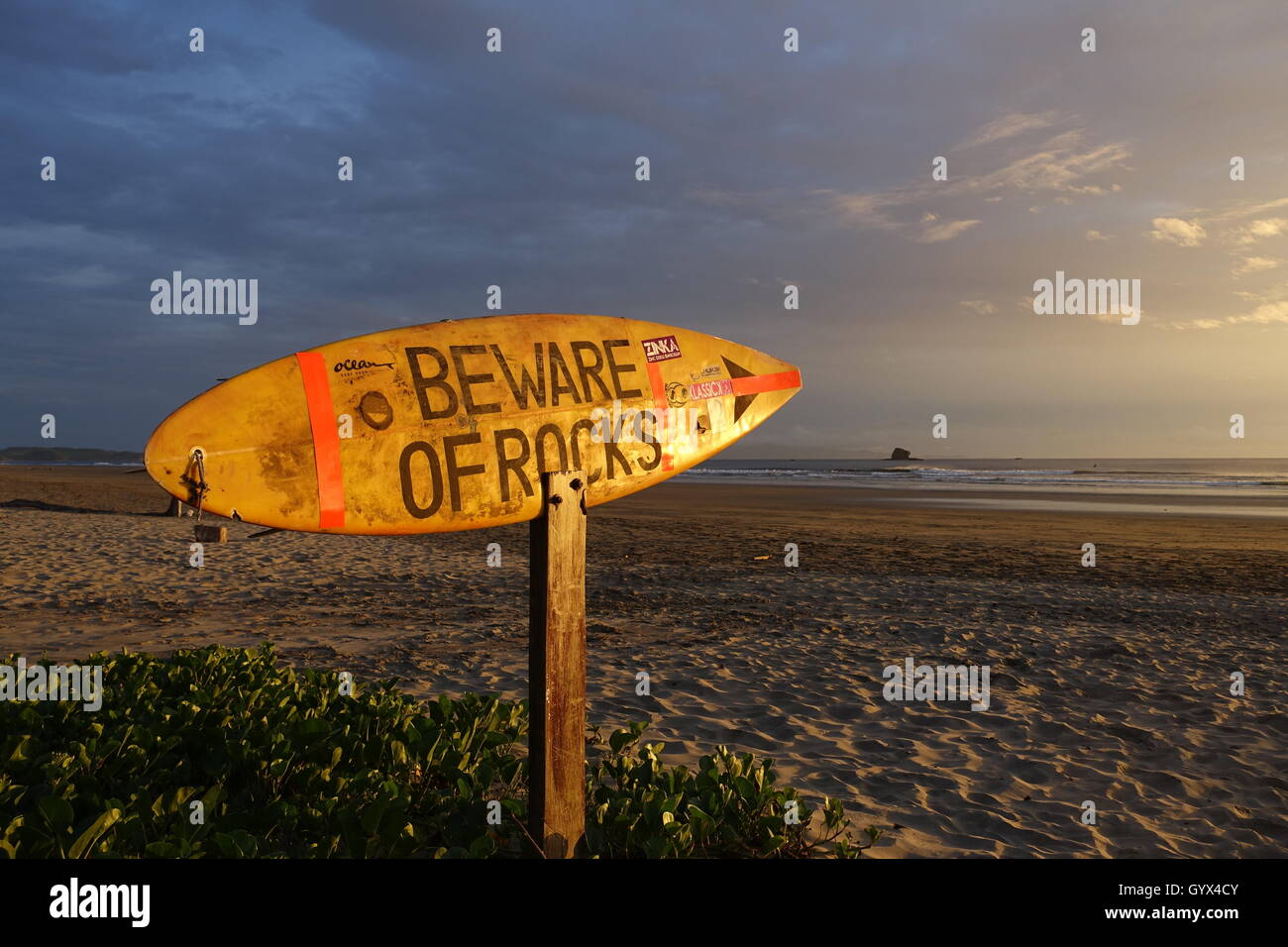 Surfbrett montiert als Zeichen am Strand bei Sonnenuntergang Warnung Vorsicht bei Felsen in San Juan del Sur, Nicaragua Stockfoto