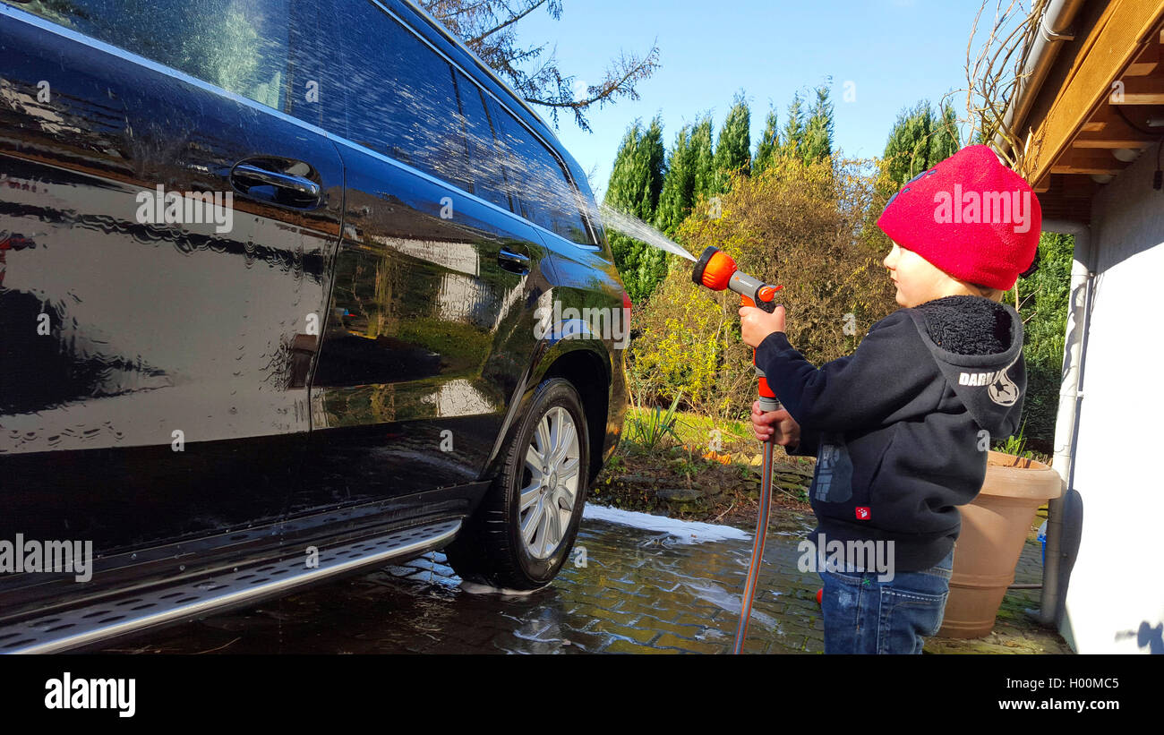 Little boy Duschen ein Auto mit einem Wasserschlauch, Seitenansicht, Deutschland Stockfoto