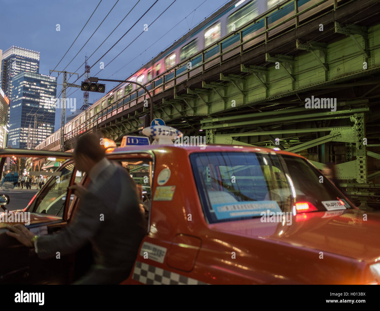 Mann immer aus ein Taxi als Yamanote Linie Passagier Zug Streifen von über ihm.   Stadtstraße nachts Yurakucho Tokyo, Japan Stockfoto