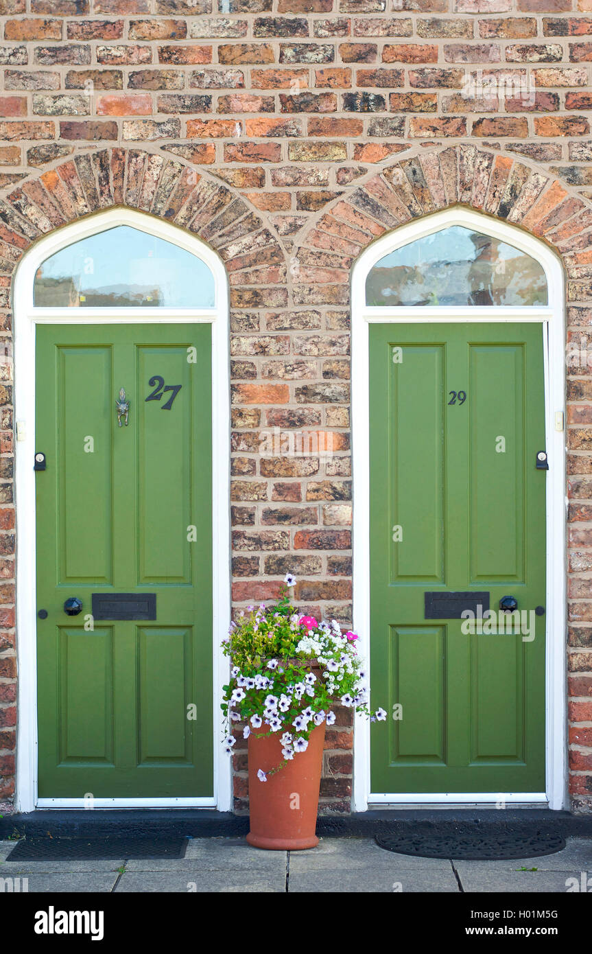 Zwei identische grüne Eingangstüren mit Blumentopf dazwischen, Bromborough Pool Garden Village Stockfoto