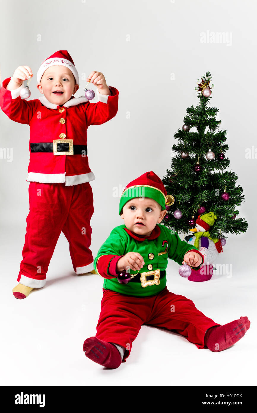 Zwei Baby-jungen verkleidet als Weihnachtsmann und Santas Helper neben Weihnachtsbaum. Weißen Hintergrund. Stockfoto