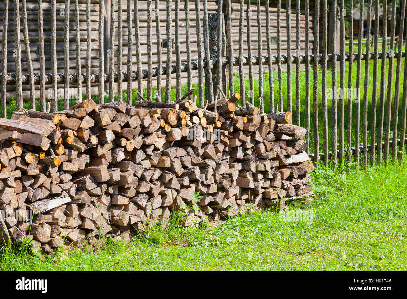 Brennholz gestapelt auf Sommergrün Rasen in der Nähe von alten ländlichen Holzzaun Stockfoto