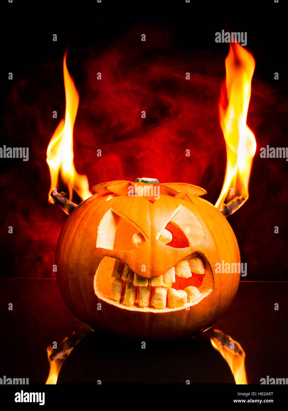 Das böse Gesicht der Halloween Kürbis mit Flammen und roten Rauch im Hintergrund. Stockfoto