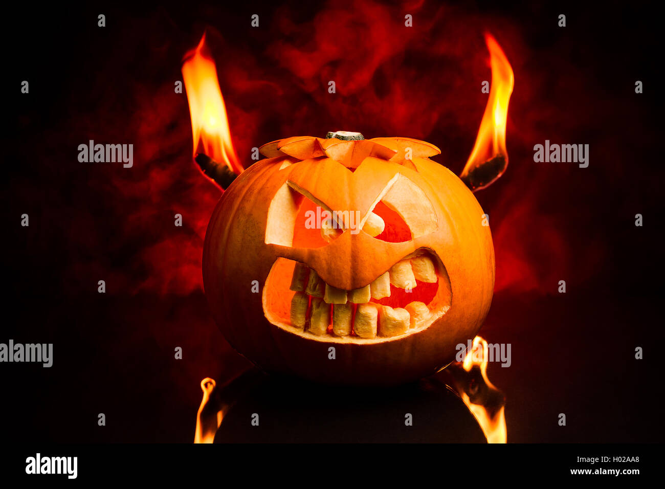 Das böse Gesicht der Halloween Kürbis mit Flammen und roten Rauch im Hintergrund. Stockfoto
