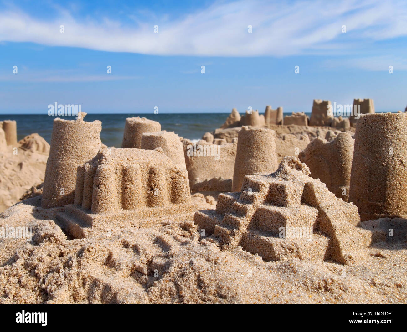 Nahaufnahme in eine Sandburg am Strand mit Meer, blauer Himmel und Wolken im Hintergrund. Stockfoto