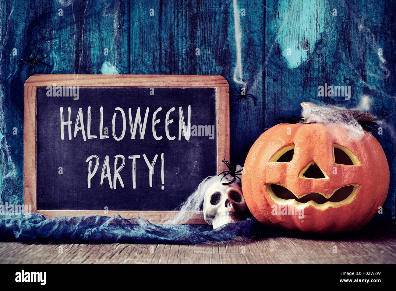 eine Tafel mit dem Text Halloween-Party, platziert auf einer rustikalen hölzernen Fläche neben einem Schädel und einem geschnitzten Kürbis mit bedeckt Stockfoto
