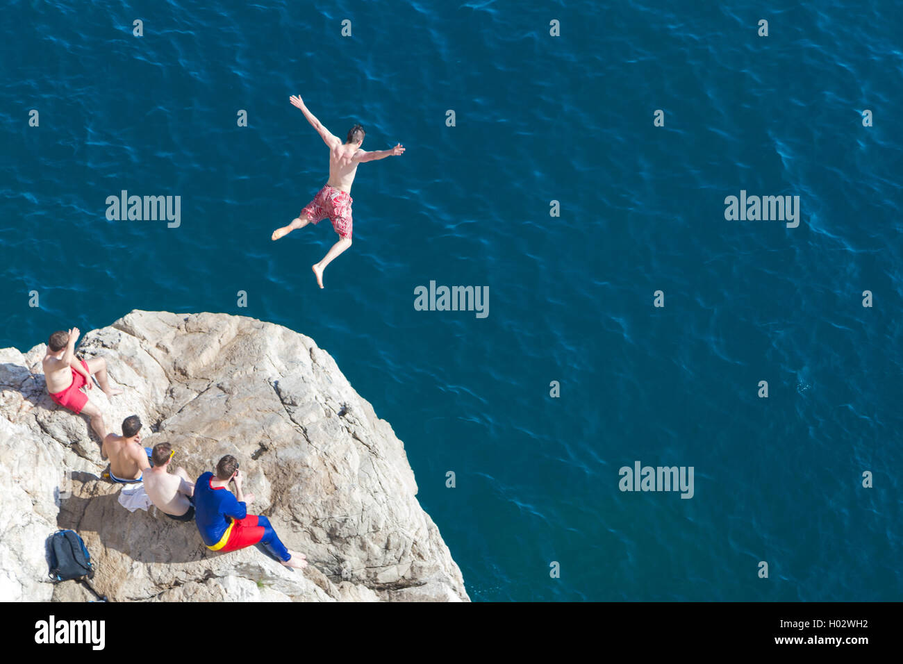 Junger Mann springt von einer Klippe ins Meer. Stockfoto