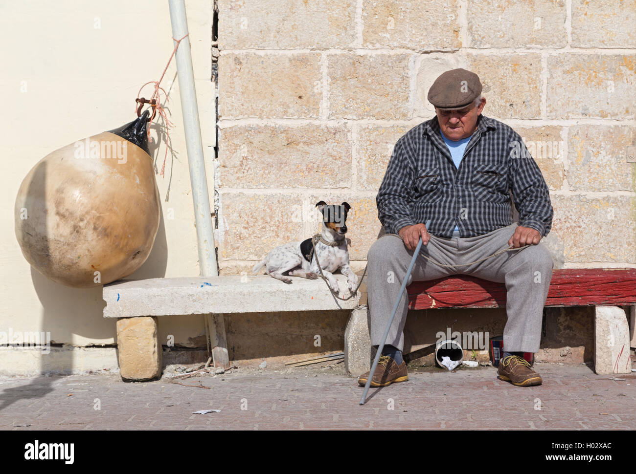 MARSAXLOKK, MALTA - 11. Januar 2015: Älterer Mann mit Hund auf der Straße Bank sitzen. Stockfoto