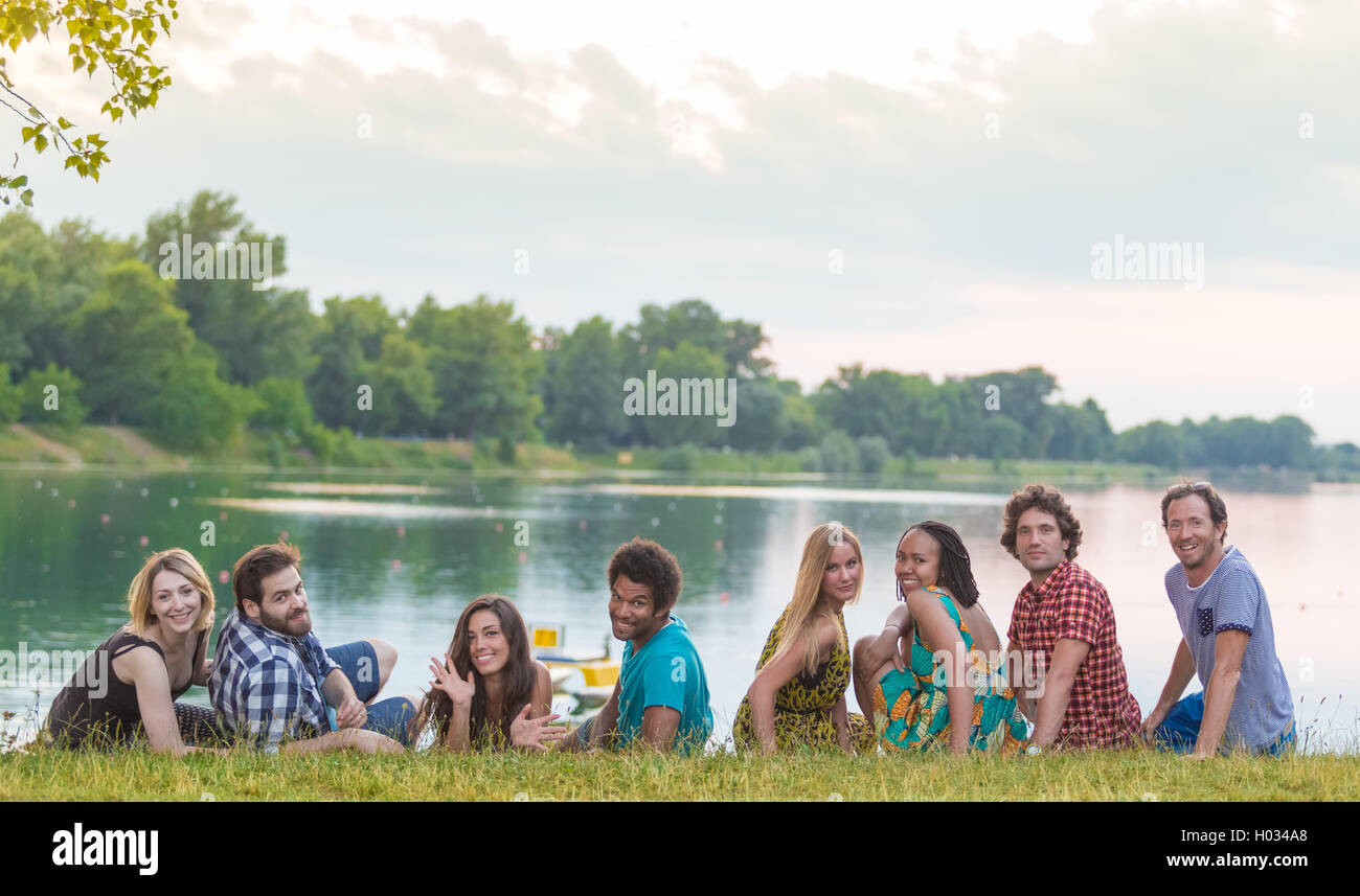 8 junge gut aussehende Erwachsene Verlegung auf dem Rasen in der Nähe von See in sommerlich fühlen Stockfoto