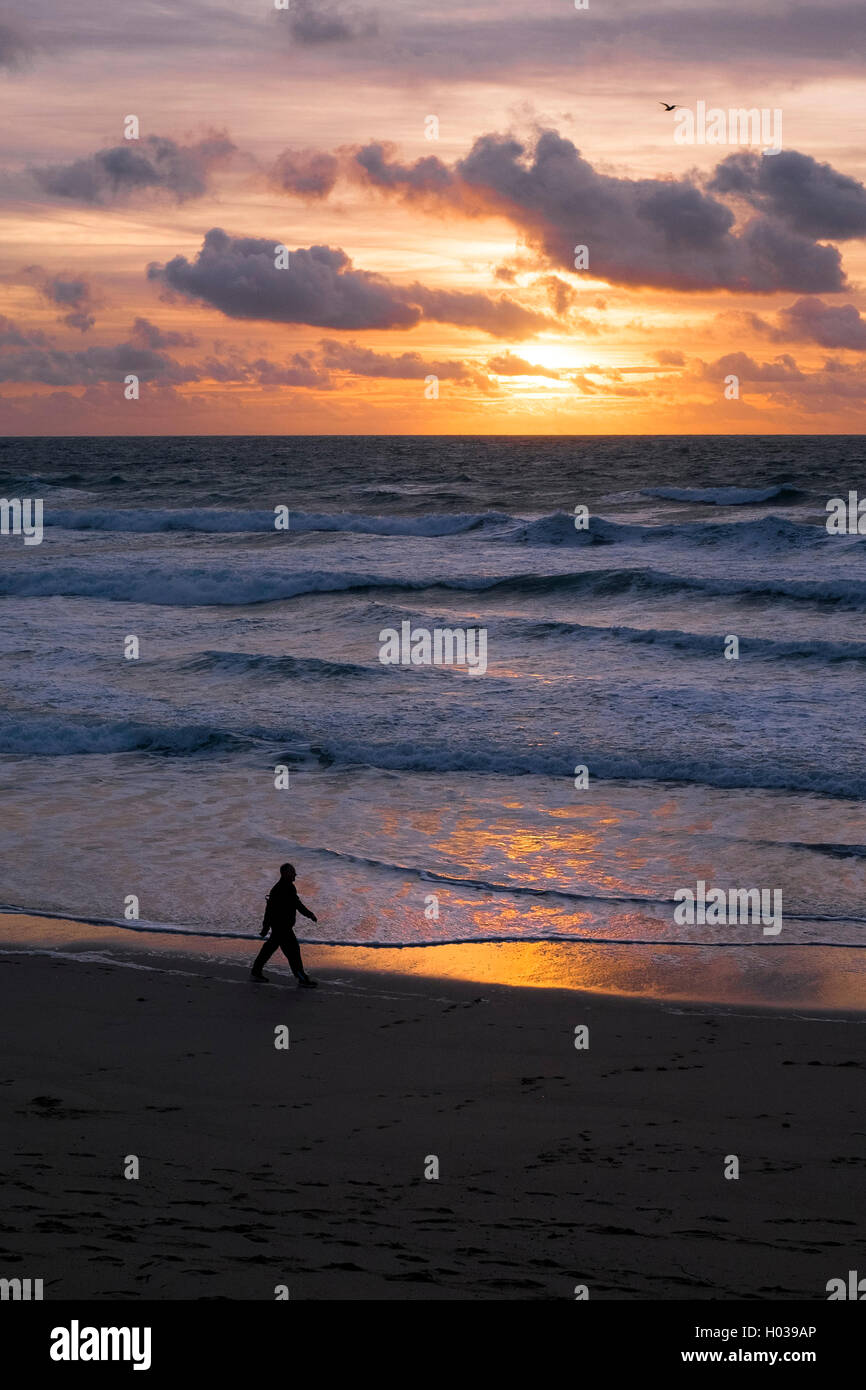 Ein Mann in der Silhouette zu sehen, wie er über Fistral Strand bei Sonnenuntergang geht. Newquay, Cornwall. Stockfoto