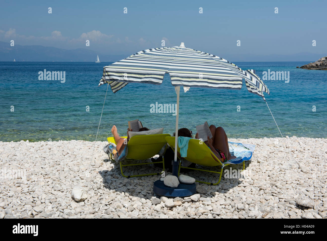 Zwei Frauen unter einem Sonnenschirm am Strand Avlaki, die Ionischen Inseln Korfu, Griechenland, Europa Stockfoto