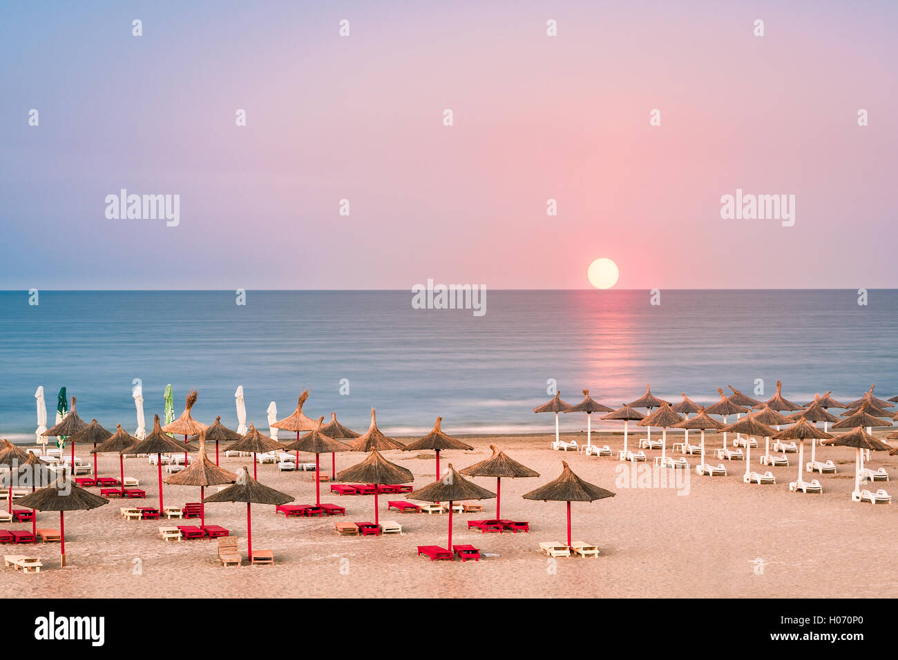 Klaren Himmel Sonnenaufgang über einen schwarzen Meer Sandstrand mit Stroh Sonnenschirme in Rumänien Stockfoto