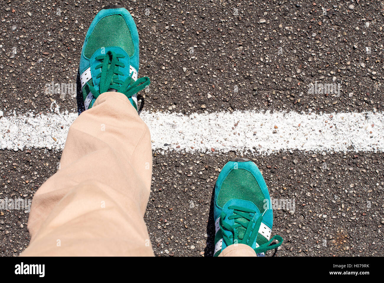 Ein paar Füße er einen Schritt auf eine asphaltierte Straße über eine weiße Linie. Konzept der Leistung. Stockfoto