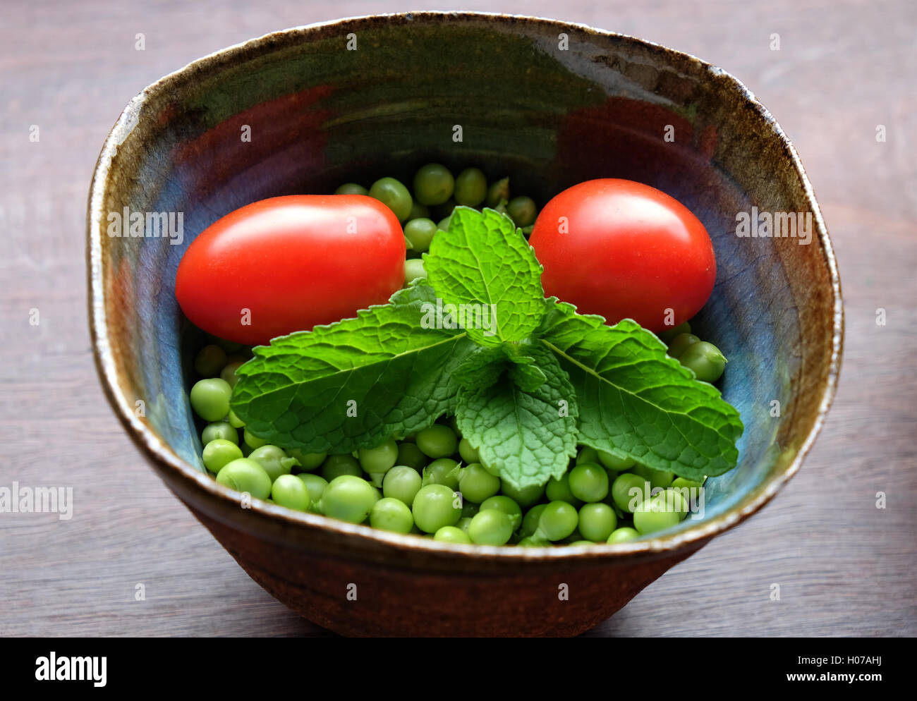 Frische Erbsen mit Minze und Tomaten in Hand geworfen Keramik Schüssel Stockfoto