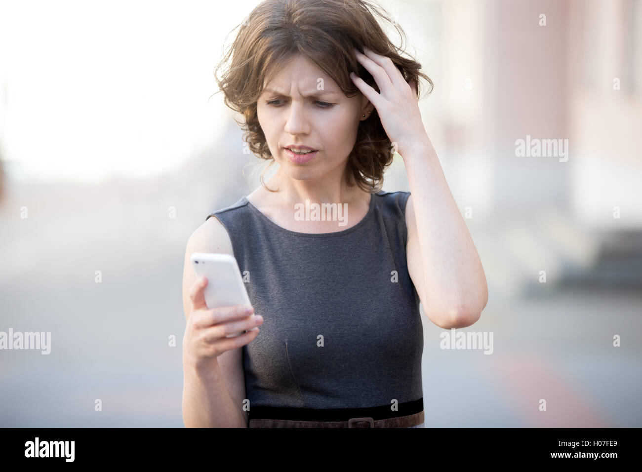 Porträt der jungen Frau mit Handy in die Hände auf der Straße im Sommer Blick auf Bildschirm mit verwirrten Ausdruck, besorgt Stockfoto