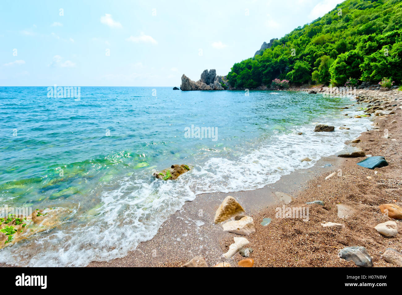 Felsenstrand, grüne Hügel, azurblaue Wasser des Meeres. Stockfoto