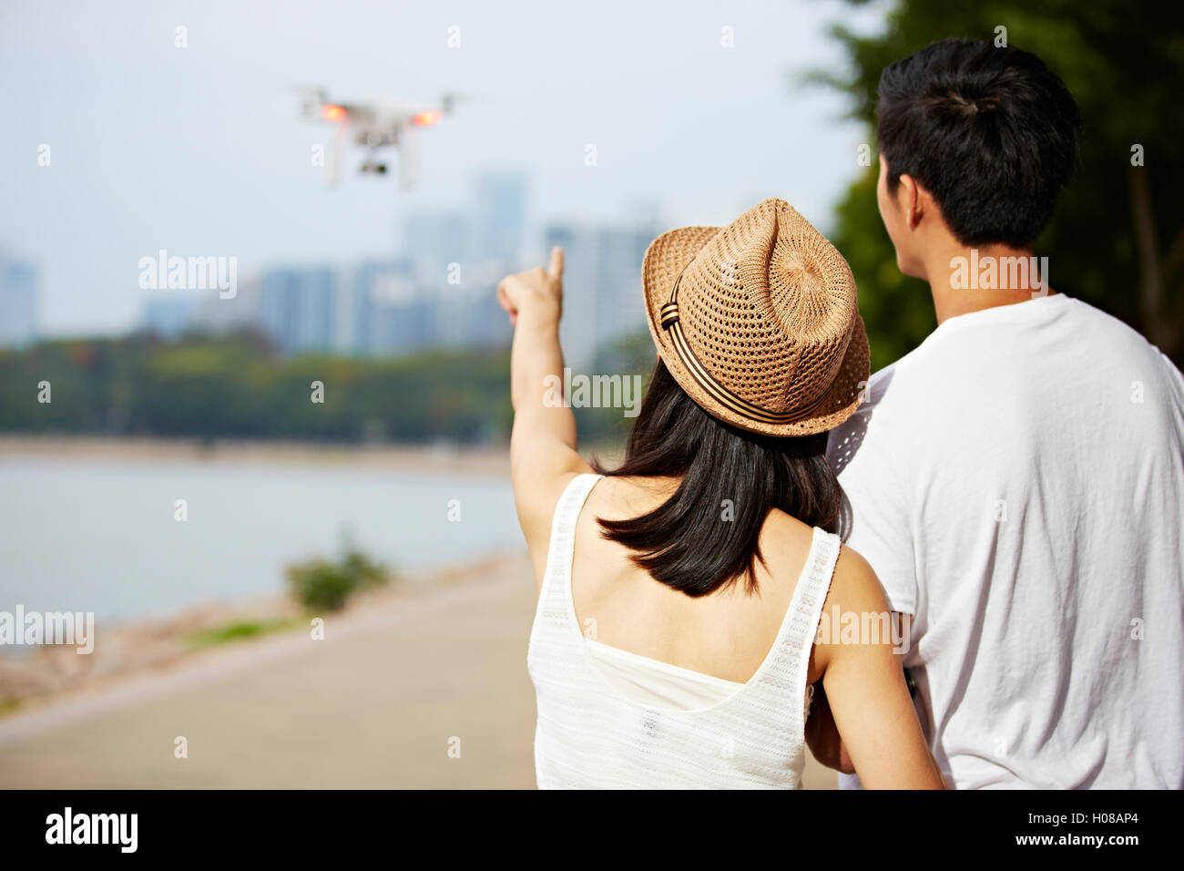 junge asiatische Frau zeigte, eine Drohne, die von ihrem Freund oder Partner betrieben Stockfoto