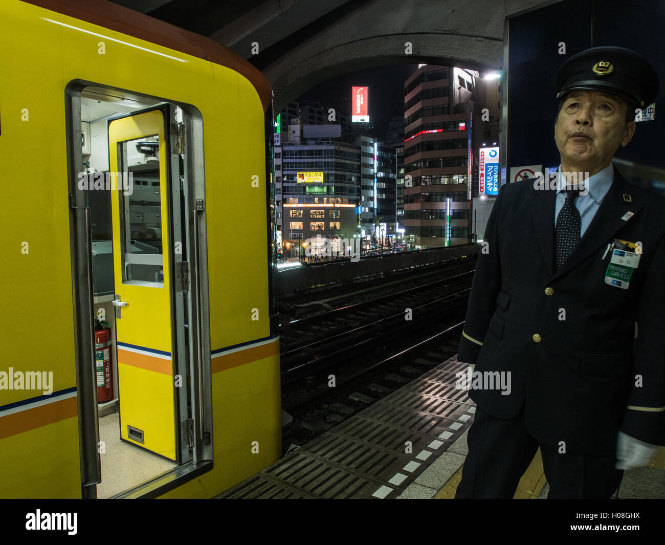 Eisenbahn-Guard prüft eine leere Plattform vor Signalisierung ok für die Ginza Line-Zug verlassen Shibuya Station Nacht in Tokio Stockfoto