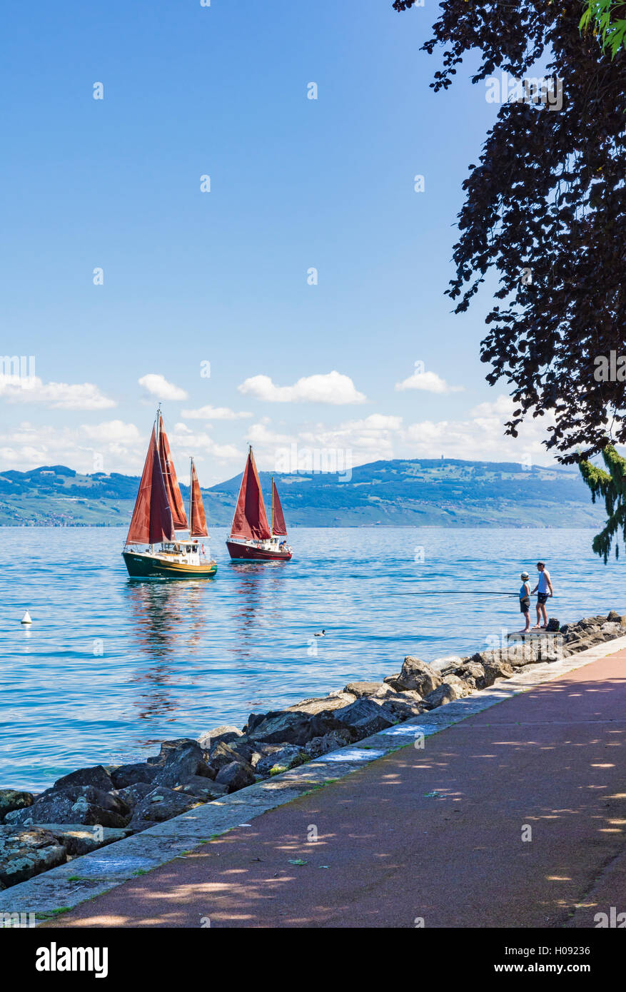 Paar, die Fischerei an der Promenade von Evian, wie traditionelle Segelboote am Genfersee, Évian-Les-Bains, Frankreich vorbeiziehen Stockfoto