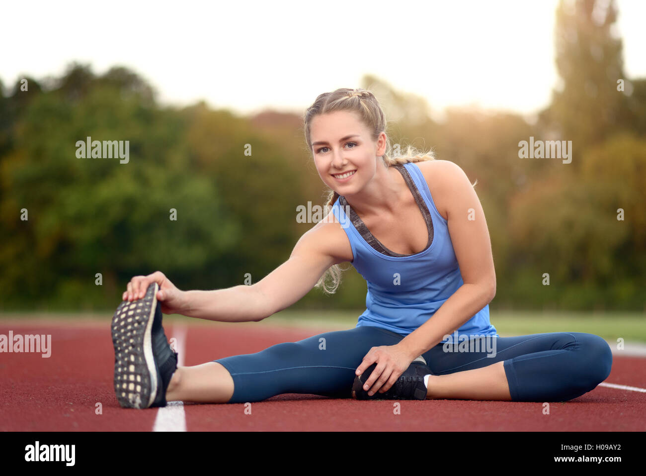 Glücklich Fit junge Frau tun stretching Übungen wie sie sitzt auf einer Leichtathletikbahn Aufwärmen vor dem Training in ein Gesundheits- und f Stockfoto