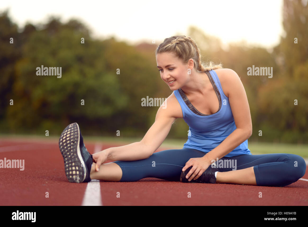 Glücklich Fit junge Frau tun stretching Übungen wie sie sitzt auf einer Leichtathletikbahn Aufwärmen vor dem Training in ein Gesundheits- und f Stockfoto