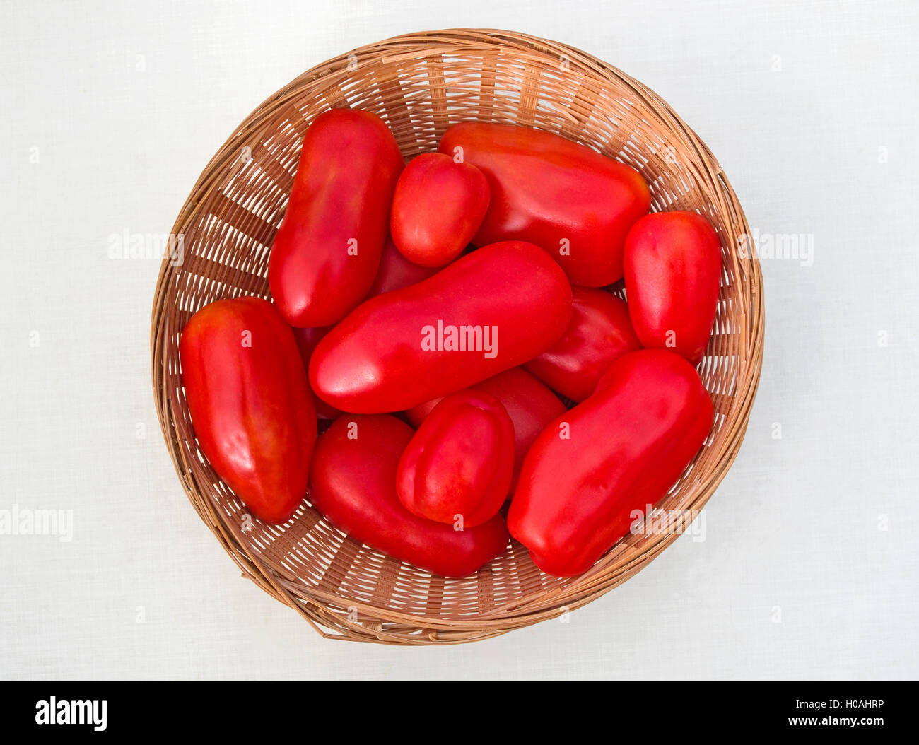 Stillleben-Anordnung der San Marzano Tomaten in runden geflochtenen Korb, weißen Hintergrund. Stockfoto