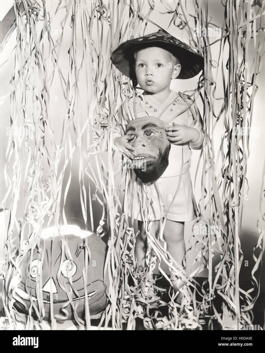 Kleiner Junge hält Maske stehen von Luftschlangen Halloween-Kostüm Stockfoto