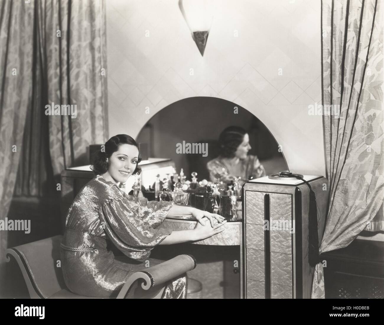 Frau in metallic-Kleid sitzt an ihrem Schminktisch Stockfoto