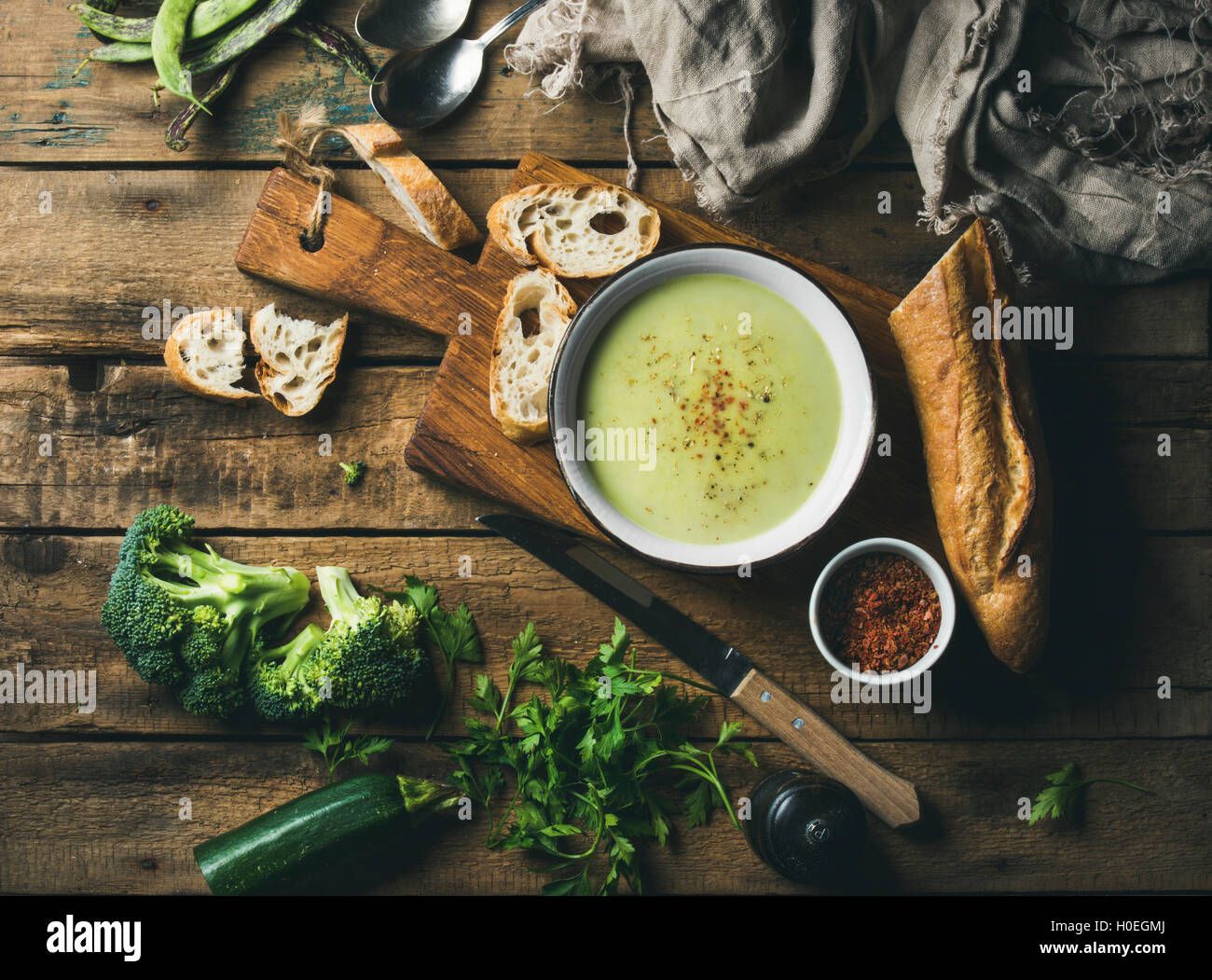 Hausgemachte Erbsen, Broccoli, Zucchini Creme Suppe in weiße Schüssel mit frischem Baguette auf Holzbrett über rustikale Hintergrund, Ansicht von oben, Stockfoto