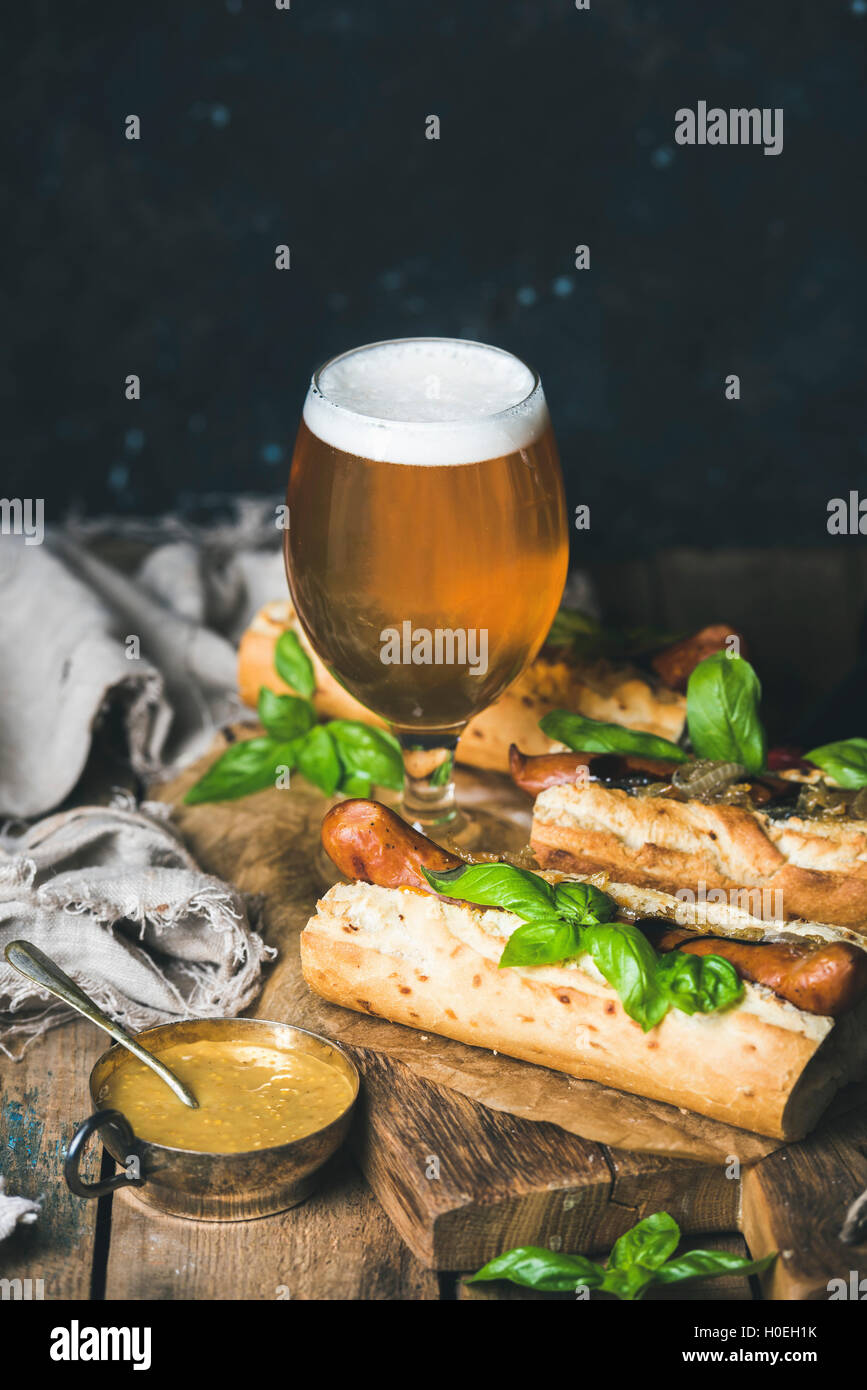 Glas Weißbier ungefiltert und hausgemachte gegrillte Wurst Hunde in Baguette mit Senf, karamelisiert Zwiebeln und Kräutern auf g Stockfoto