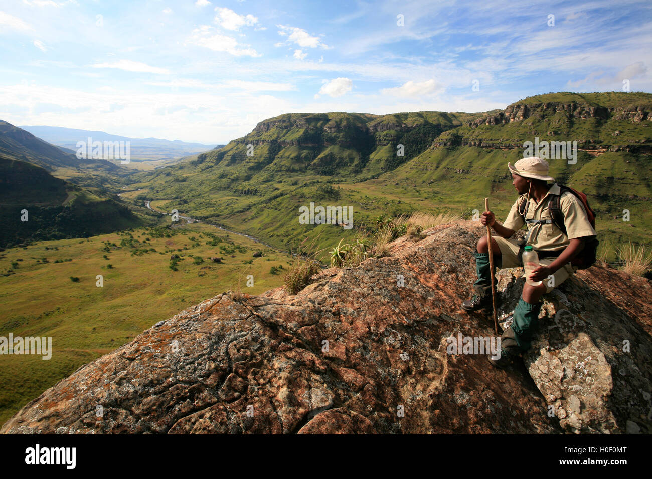 Eine Anleitung, sitzt auf einem Felsen mit Blick auf das eMhlawazini Tal En Route zu den Eland-Höhle in den Drakensbergen Stockfoto