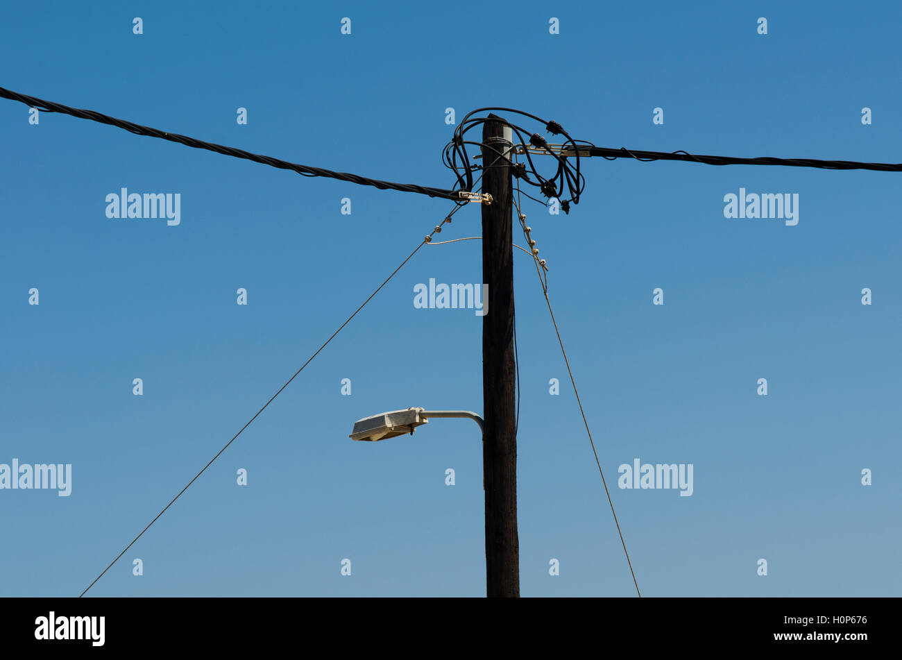 Stromleitung auf Holzmasten mit Straßenlaterne am Hintergrund blauer Himmel Stockfoto