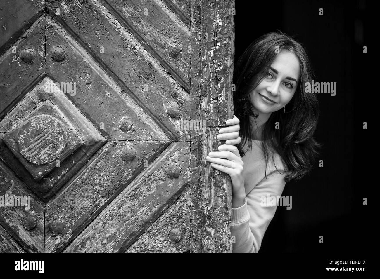 Hübsches junges Mädchen peering hinter alten Holztür, schwarz-weiß-Foto. Stockfoto