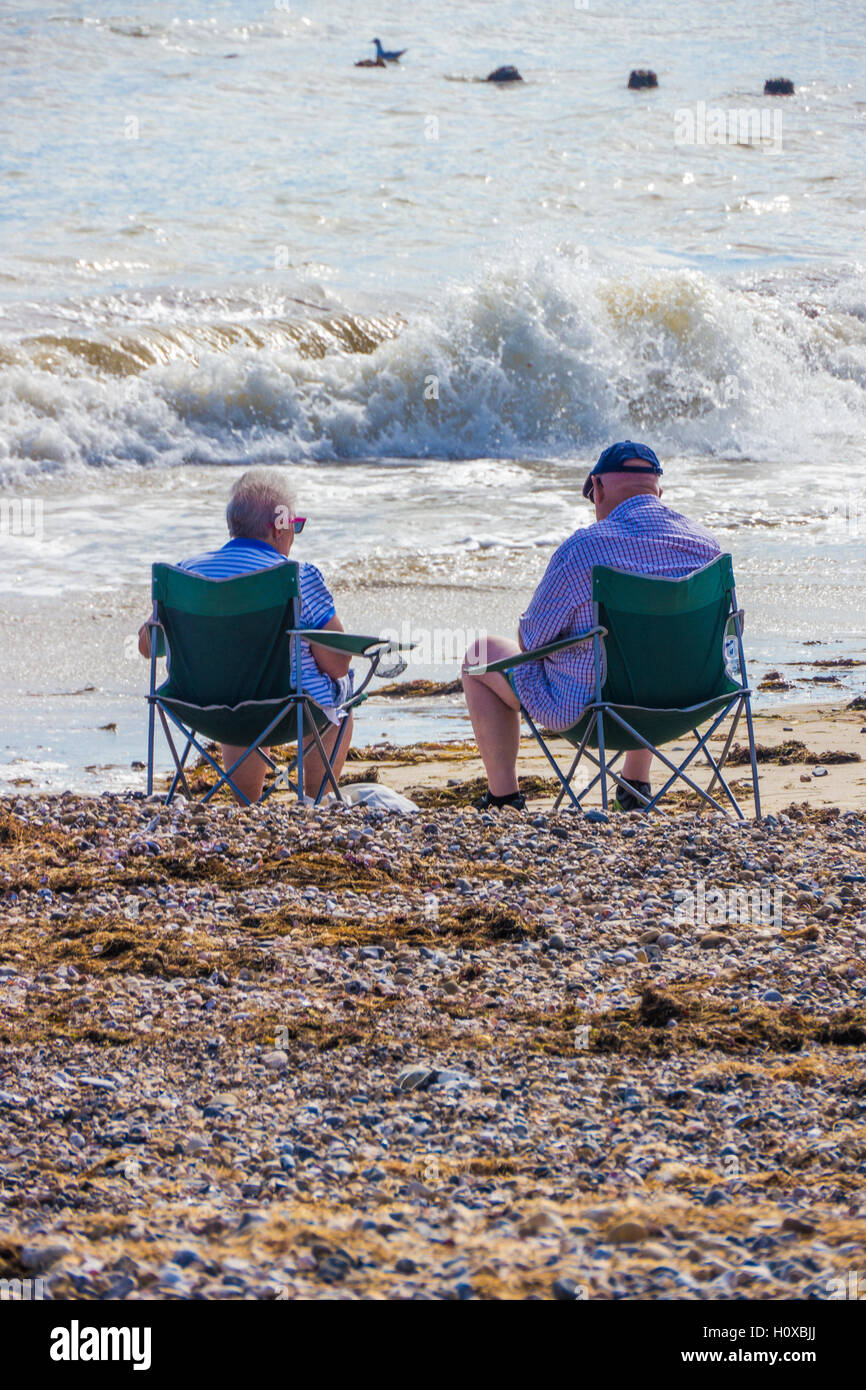 Älteres Ehepaar am Strand mit Wellen, die vor ihnen sitzen. Stockfoto