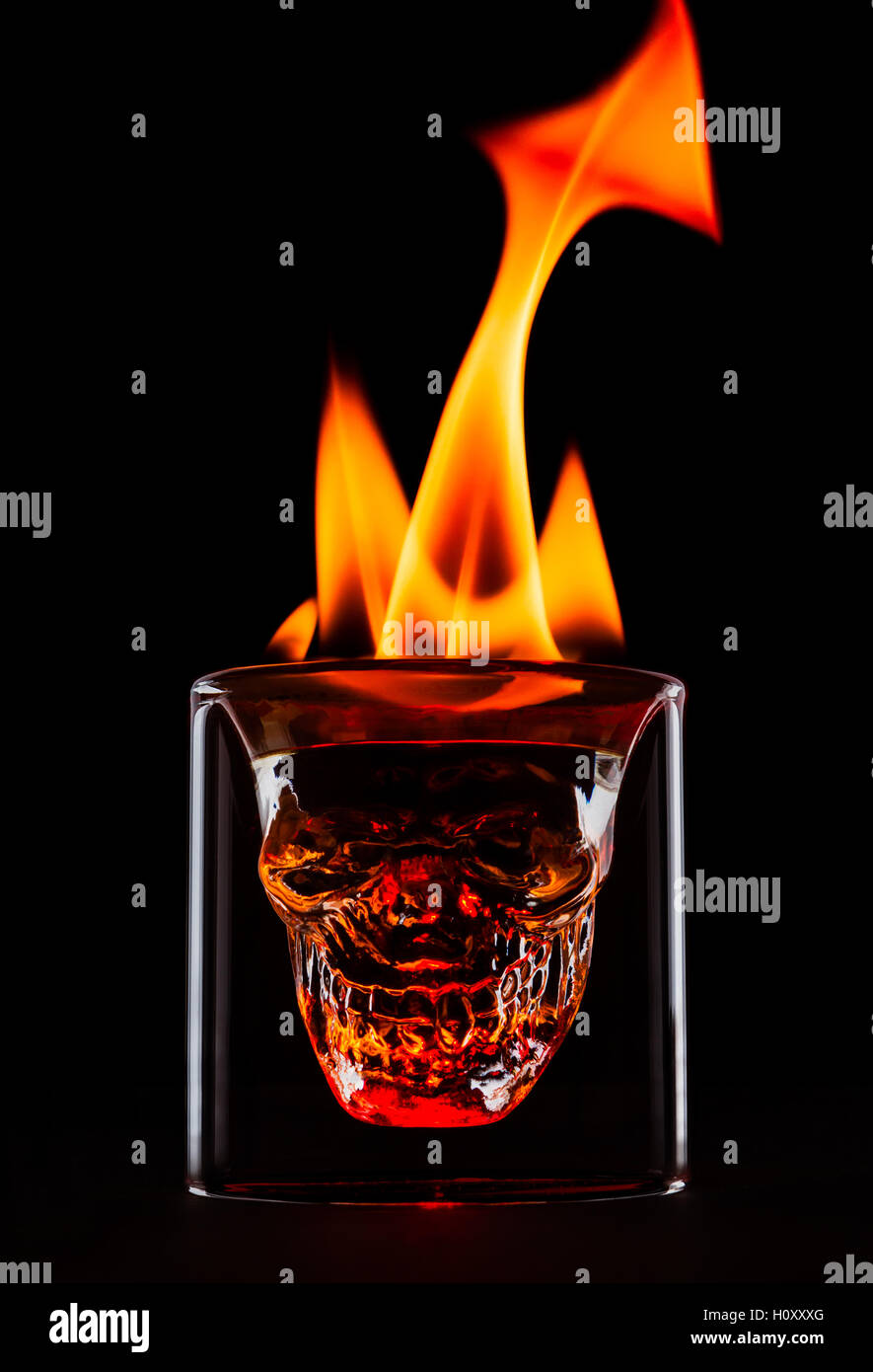 Schädel-Form-Glas mit Flammen auf der Oberseite. Einzelnes Objekt auf schwarzem Hintergrund. Feuer als die Form, Schwanz und Hörner. Dunkel und stimmungsvolle Bild des Getränks. Stockfoto