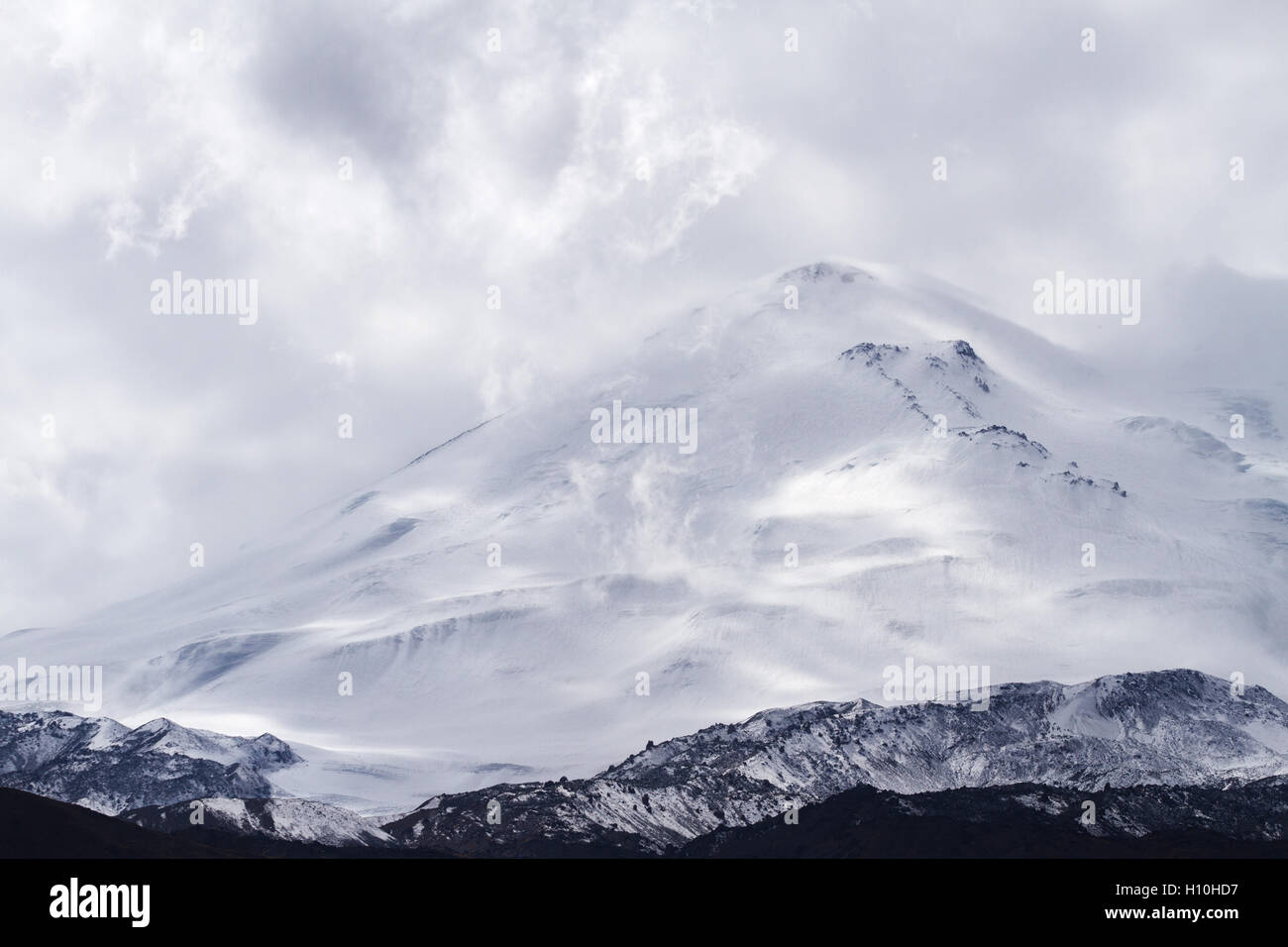 Schneebedeckten Elbrus Berg umgeben von Wolken erhebt sich über das Berggebiet in Kabardino-Balkarien (Kaukasus, Russland). Stockfoto