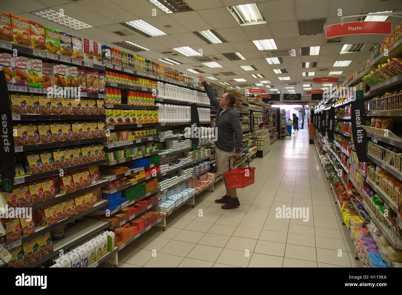 Ein Shopper erreichen um etwas aus dem obersten Regal in einen gut sortierten Supermarkt in Kasane auswählen Stockfoto