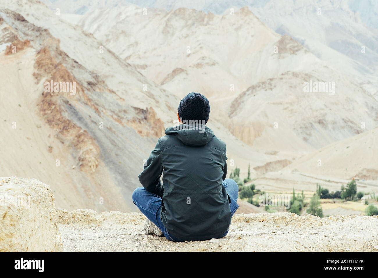 Jungen männlichen Reisenden sitzen auf der Sand Klippe, denken über etwas in Leh, Ladakh, Indien. Stockfoto