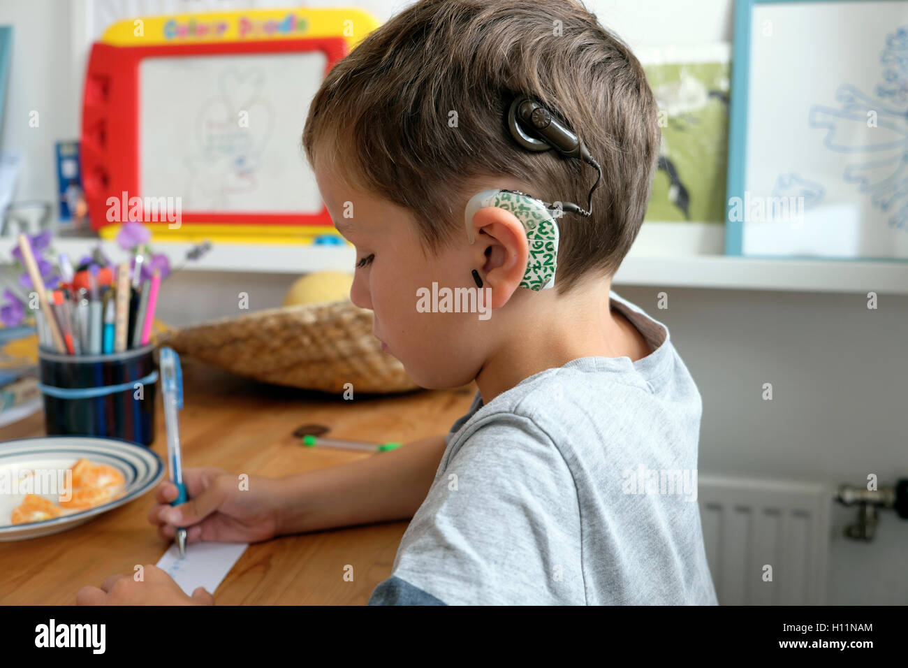 Junge gehörlose Junge Kind Kind mit Cochlea-Implantaten Implantat im Alter von 6 Jahren Zeichnen mit Pen-Papier sitzend zu Hause in Großbritannien UK KATHY DEWITT Stockfoto
