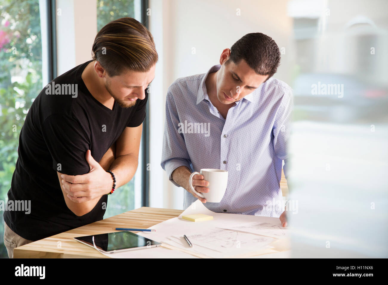 Zwei männliche Mitarbeiter in einem modernen Büro an Designs auf Papier zusammen Stockfoto
