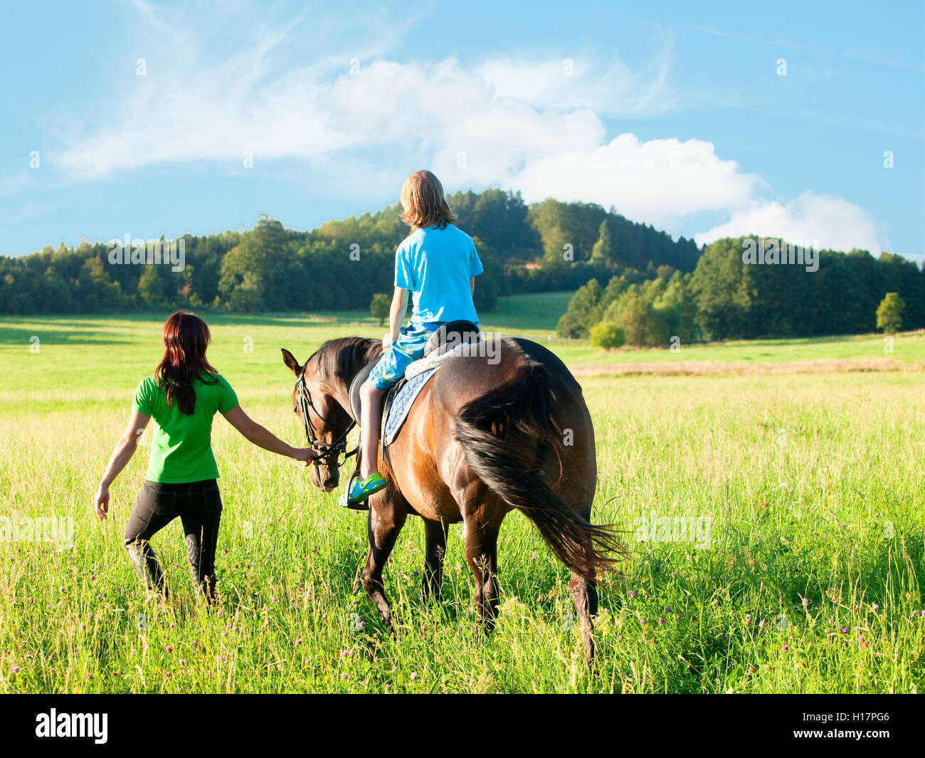 Reitstunden - Frau führt ein Pferd mit einem jungen im Sattel Stockfoto