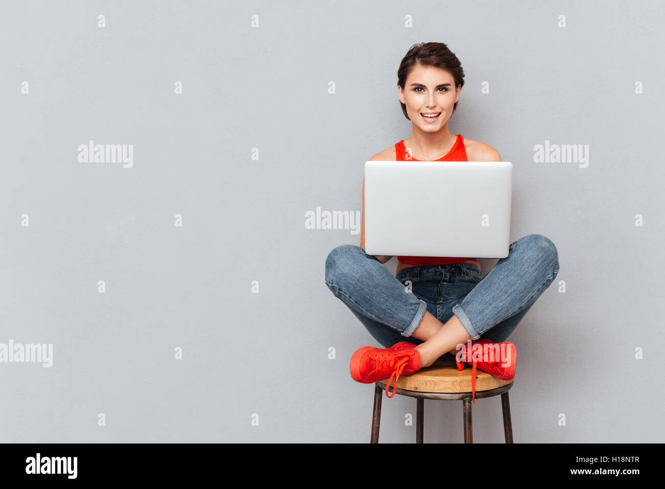 Junge schöne lächelndes Mädchen mit Laptop pc Computer für Studie auf den grauen Hintergrund isoliert Stockfoto