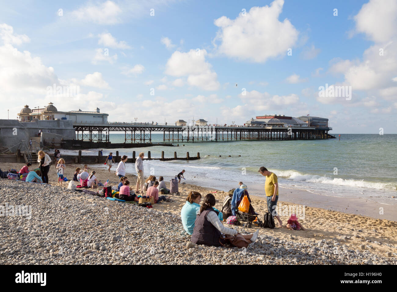 Englischer Sommer; Leute sitzen am Cromer Strand, mit Cromer Pier, Cromer, Nord Norfolk Küste, Norfolk UK Stockfoto