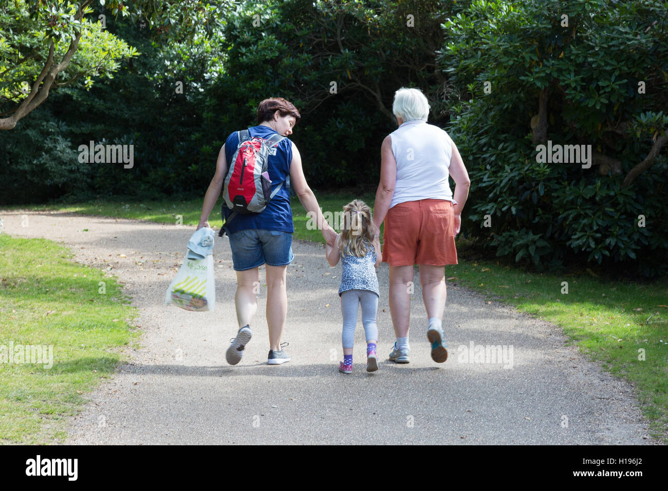 Drei Generationen von Frauen; Kind, Mutter und Großmutter, die in einem Park spazieren, von hinten gesehen, Großbritannien - Mehrgenerationenfamilie. Stockfoto