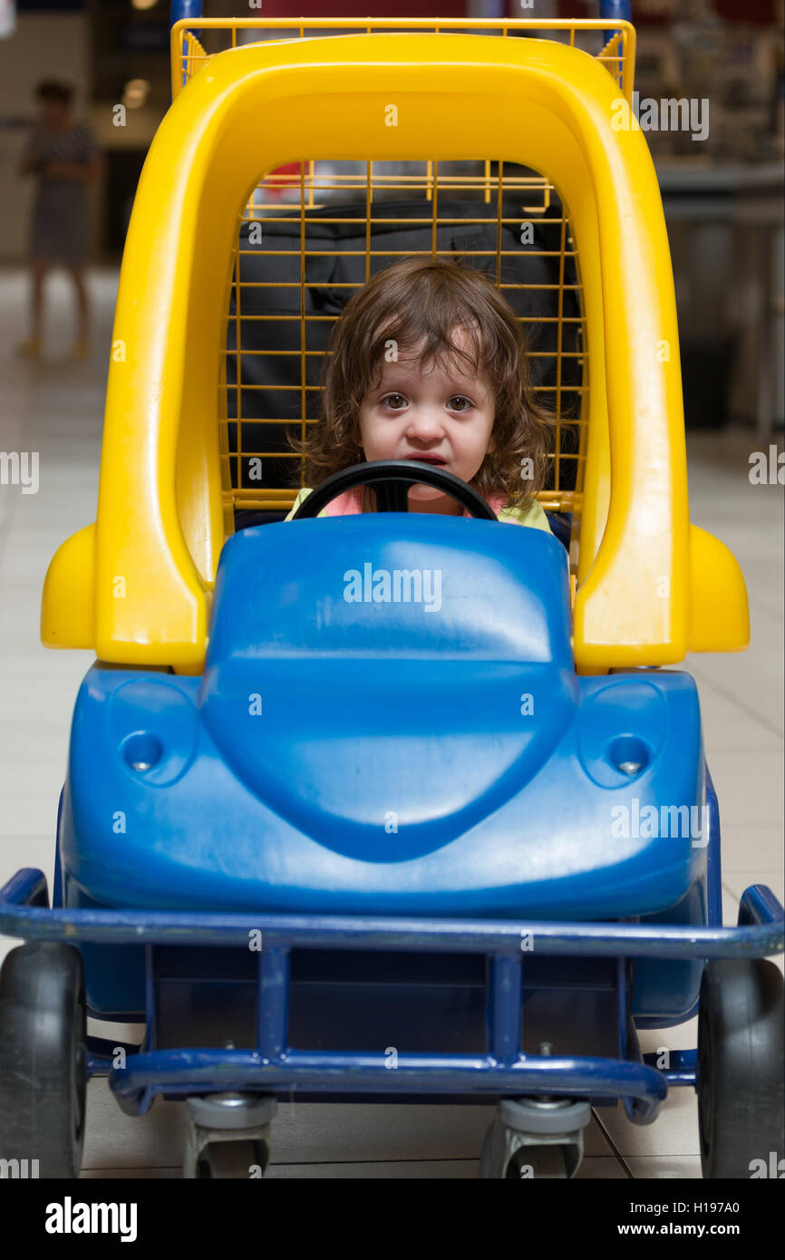 kleines Mädchen sitzt in der Kinder Maschine in einem Einkaufswagen Stockfoto