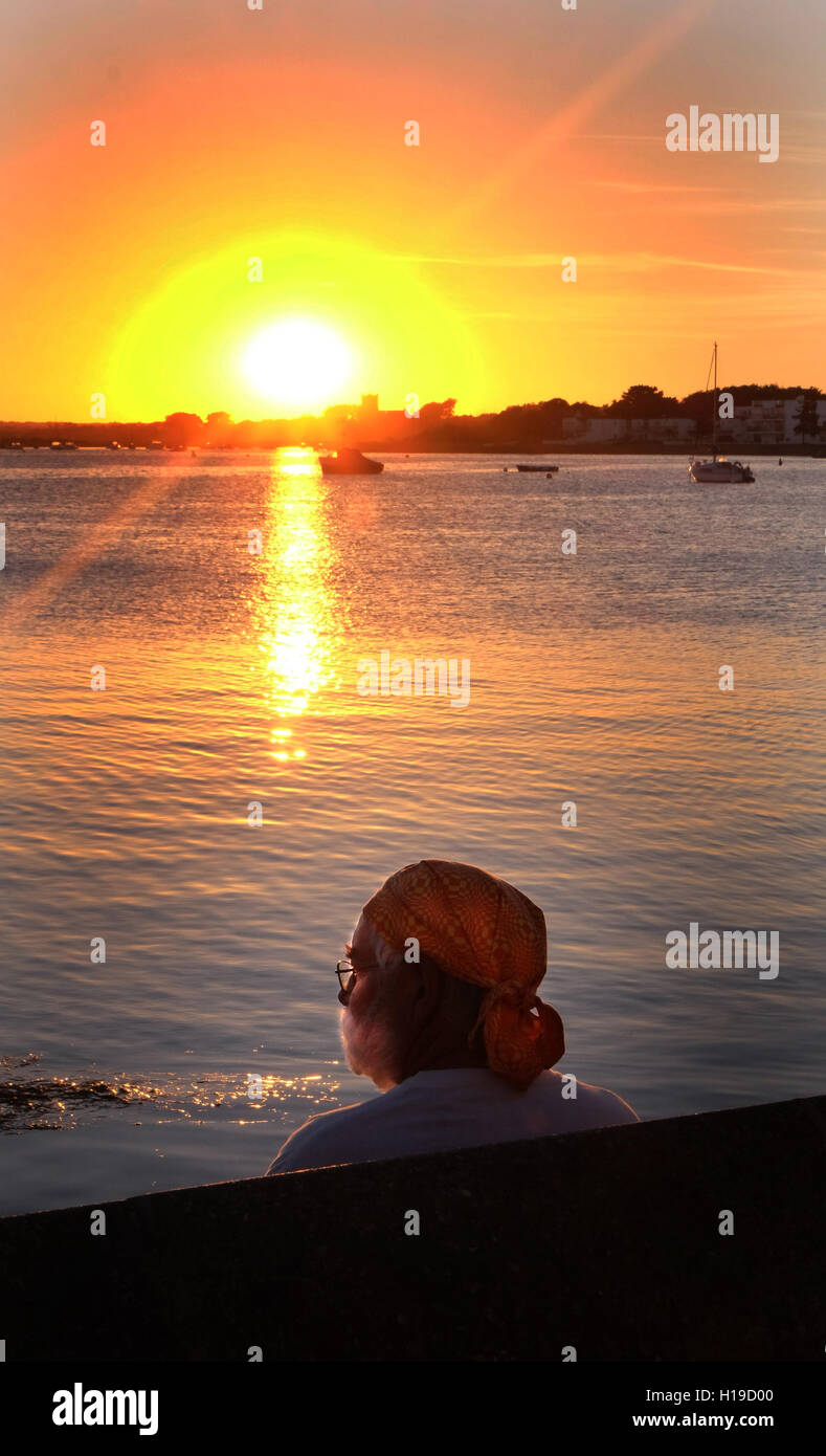 Atemberaubenden Meer Sonnenuntergang, Mann beobachtet den Sonnenuntergang am Meer, Mudeford Quay, Dorset, UK. Stockfoto