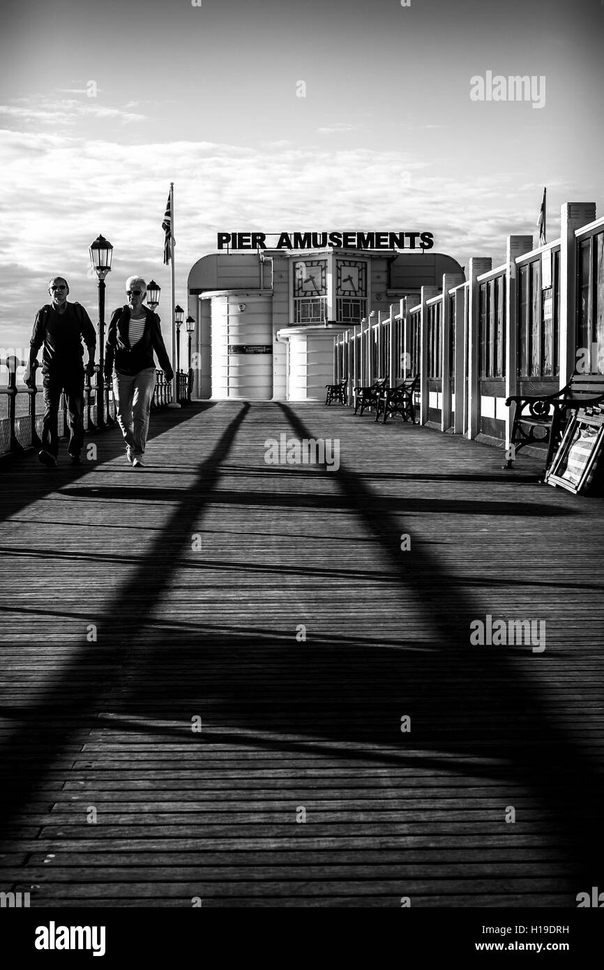 Ein paar gehen als "Leading Lines" Schatten von einem Geländer einen Pfad zu erstellen, auf der Terrasse von Worthing Pier Stockfoto