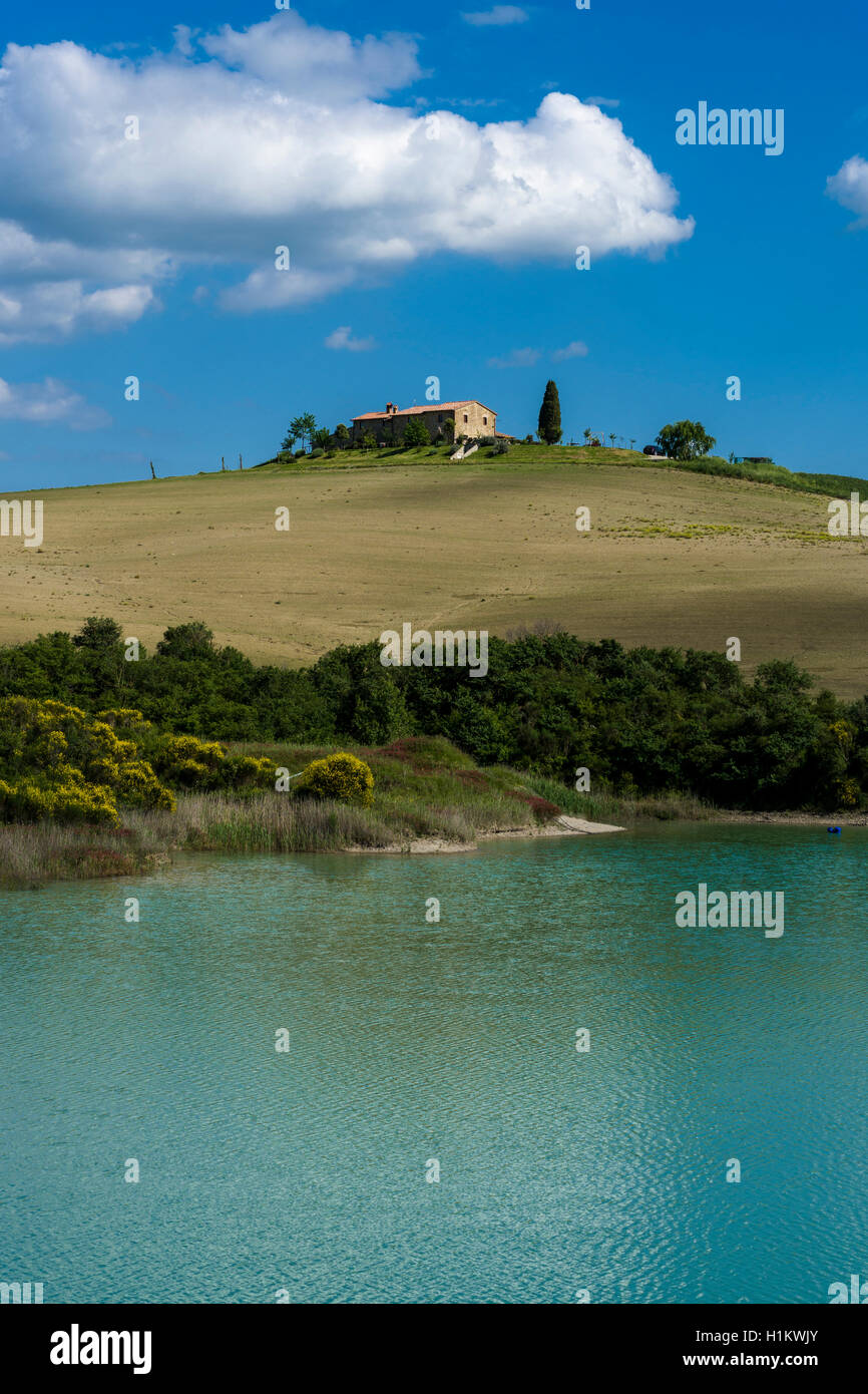 Typische Grün der toskanischen Landschaft im Val d'Orcia, Bauernhof auf einem Hügel, den See und den blauen bewölkten Himmel, La Foce, Toskana, Italien Stockfoto