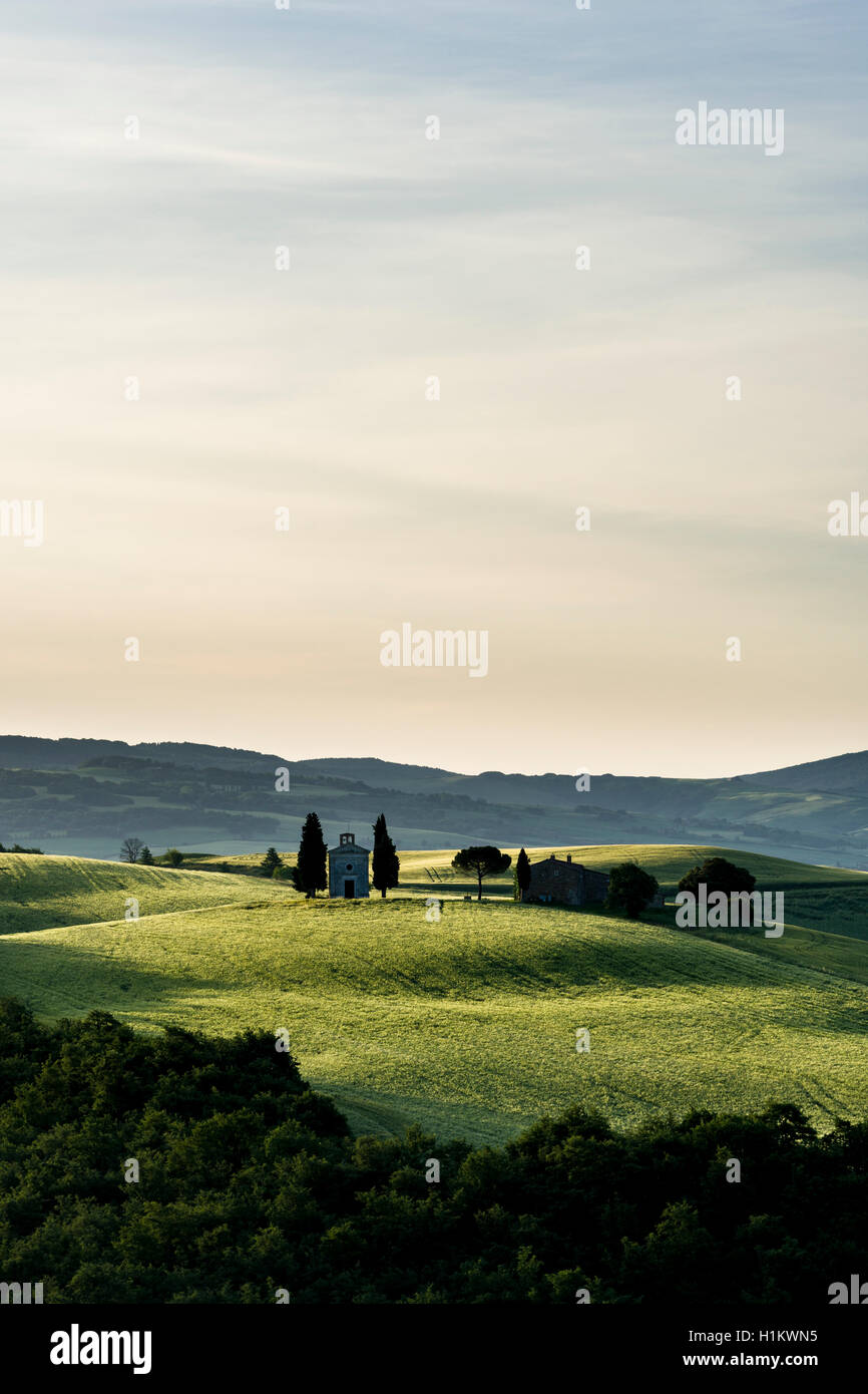 Typische Grün der toskanischen Landschaft im Val d'Orcia mit Hof und Kapelle auf einem Hügel, Felder, Zypressen, Bäume, blau, bewölkter Himmel Stockfoto