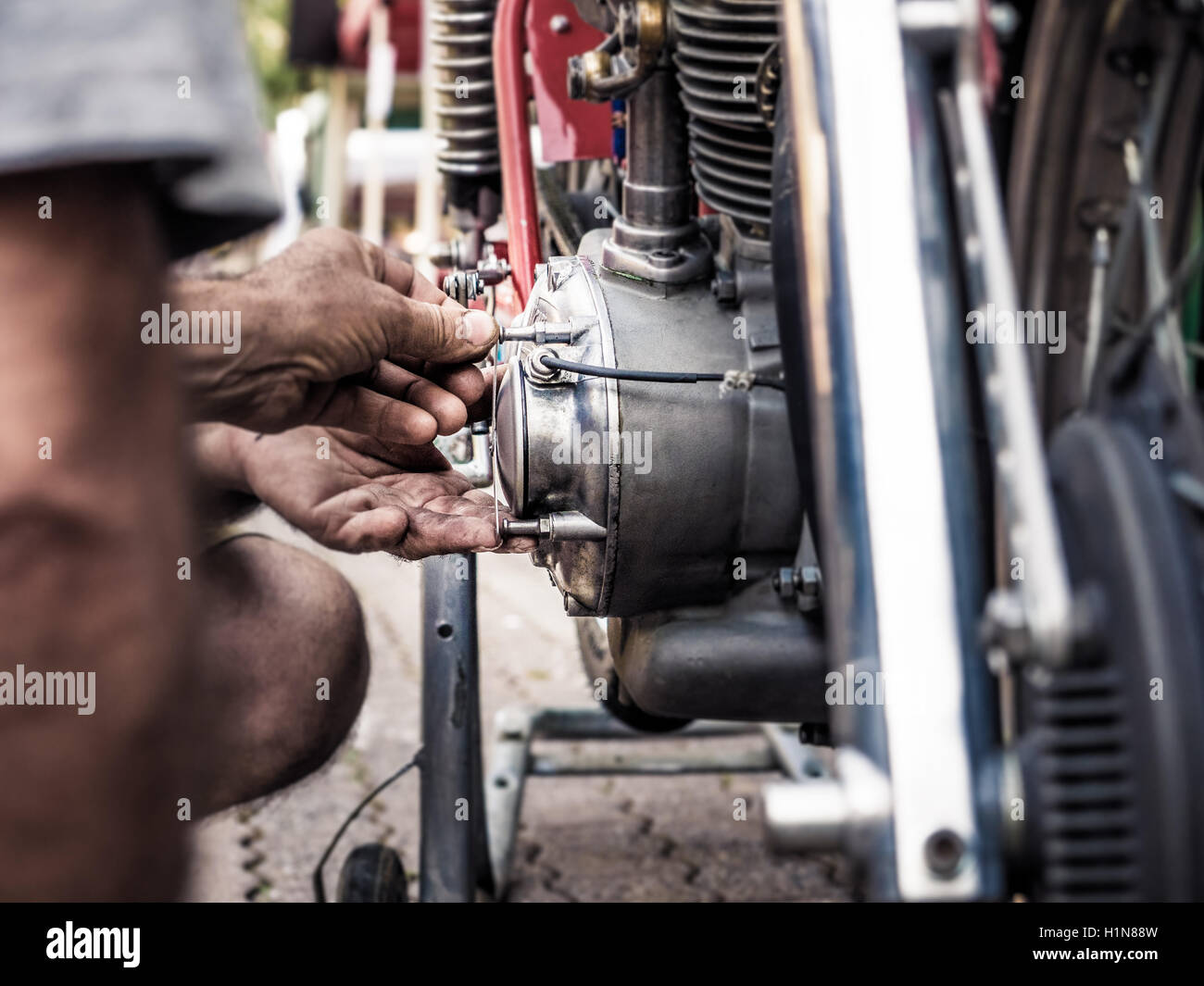 Mechaniker mit schmutzigen Händen Befestigungsschraube auf einem alten Fahrrad Motor, absichtlichen Unschärfe und lebendige Farben. Stockfoto